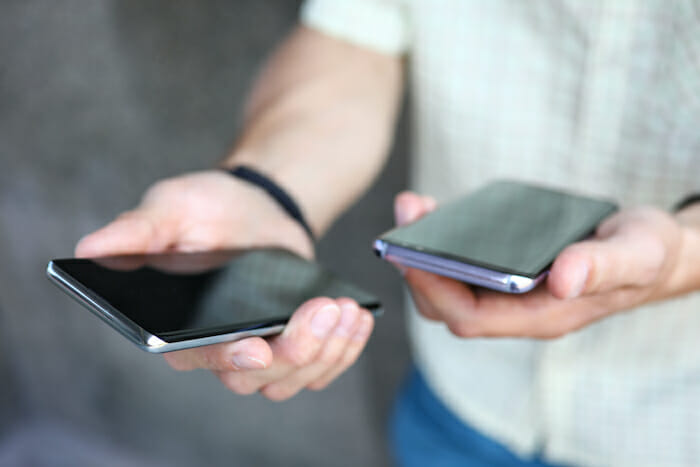 有料のマッチングアプリを使っている男性が手に携帯電話を2つ持っている様子