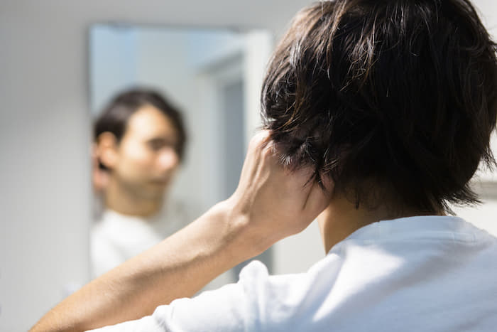 自分磨きのために鏡を見て髪の毛をセットしている男性